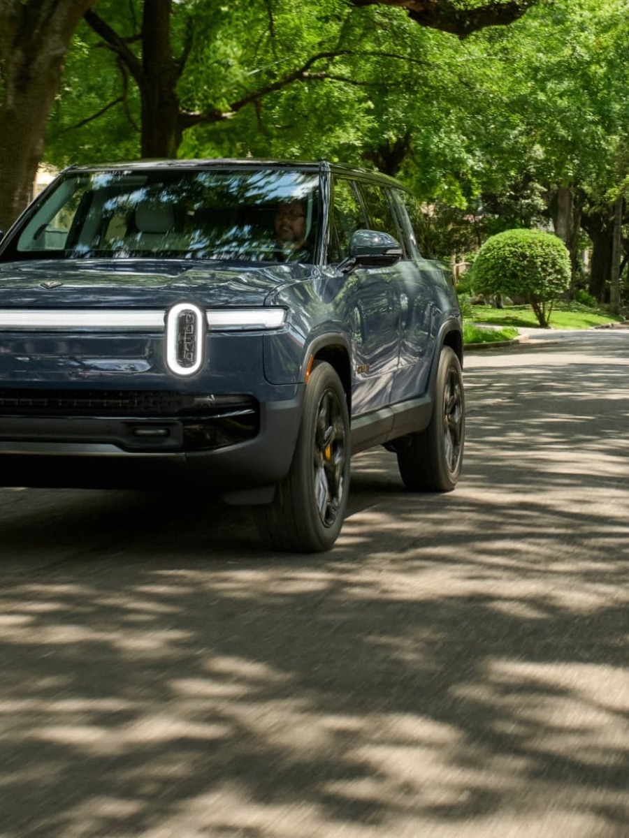 A Rivian electric vehicle driving down a tree-lined street